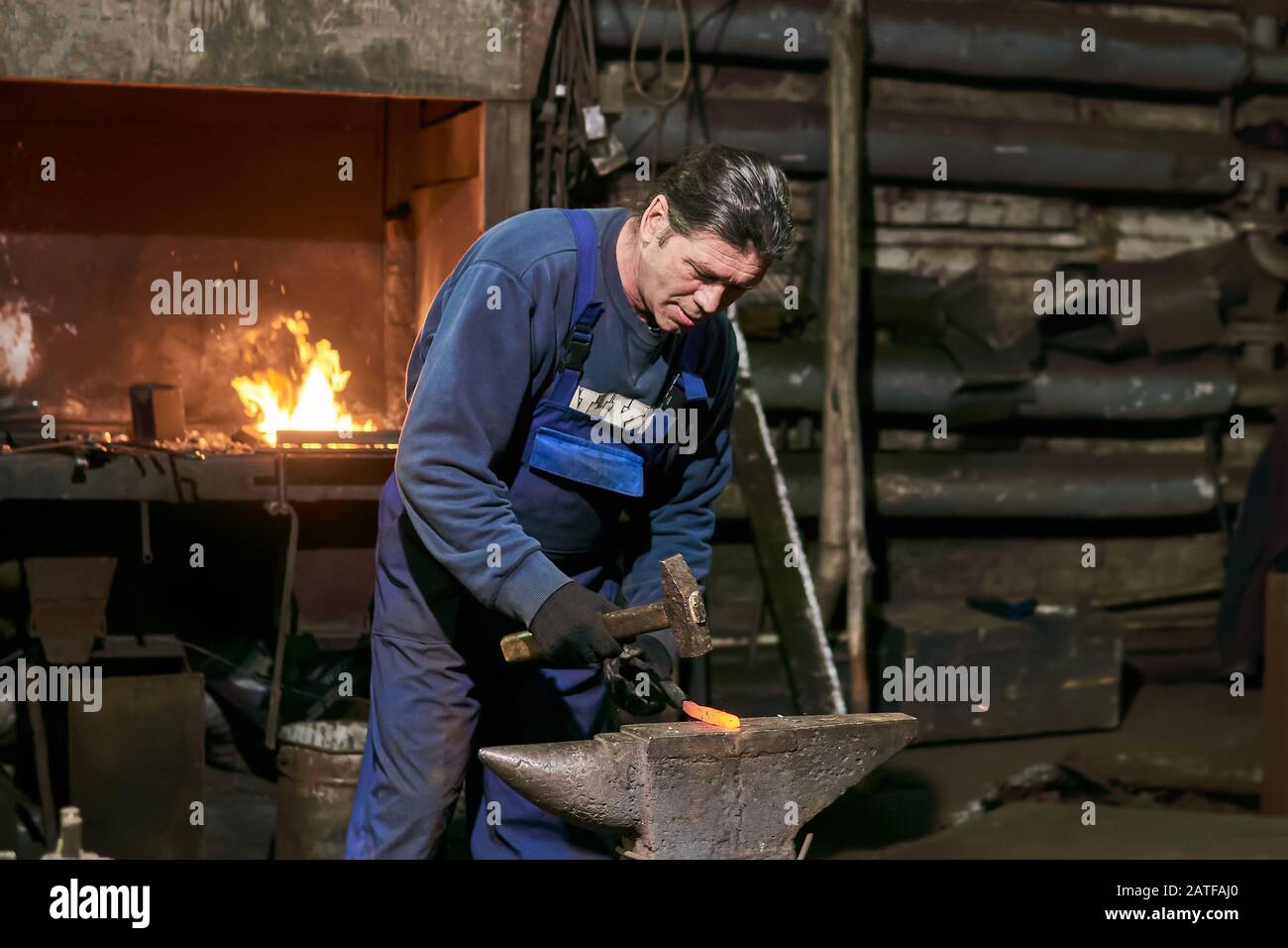 mature man blacksmith at work forges a red-hot piece of metal Stock Photo