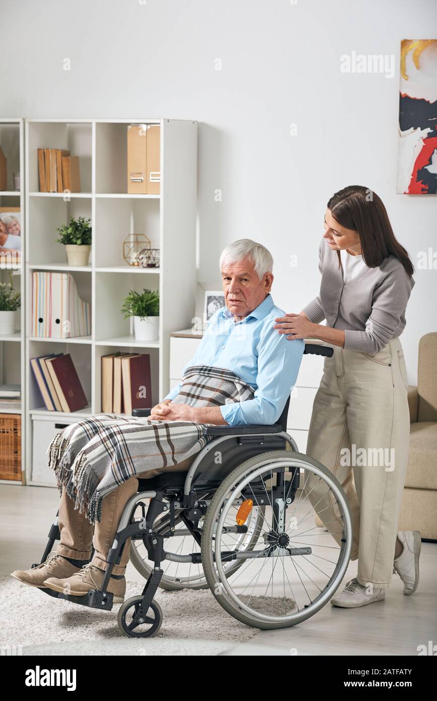 Young female care giver talking to senior male pensioner in wheelchair Stock Photo