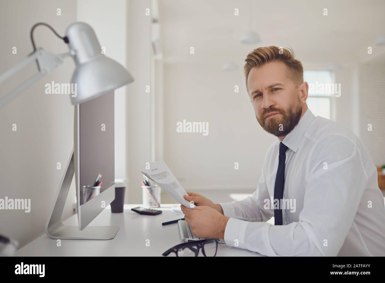 Portrait of a serious busy business man bearded sitting at a table with computers in the office. Stock Photo