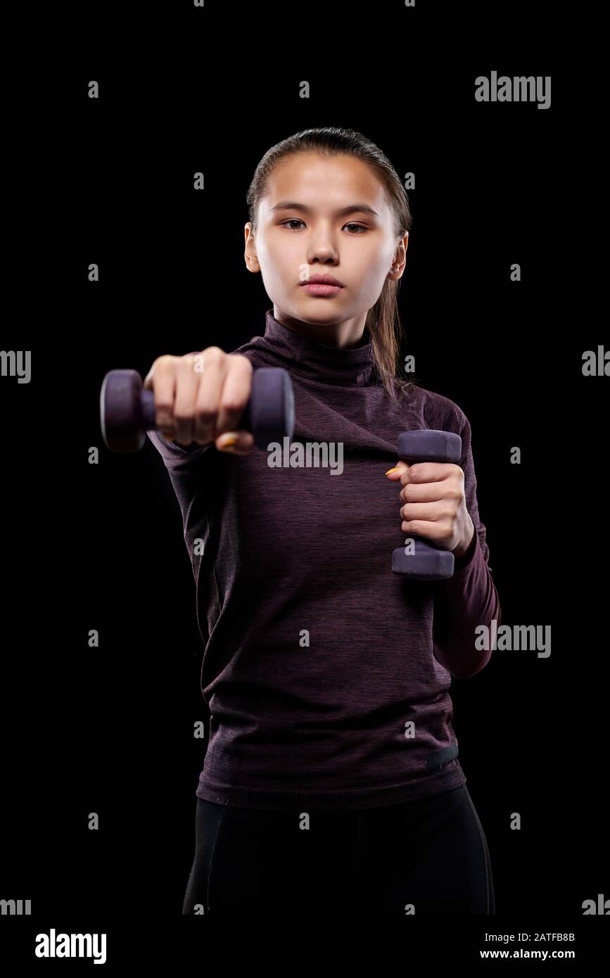 Young active female with dumbbells stretching arm forwards while exercising Stock Photo