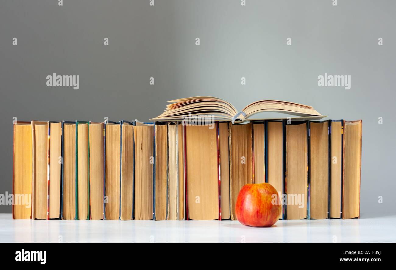 Open hardback book, diary, fanned pages on stack of books on white table with red apple. Books stacking. Back to school concept. Copy Space. Education Stock Photo