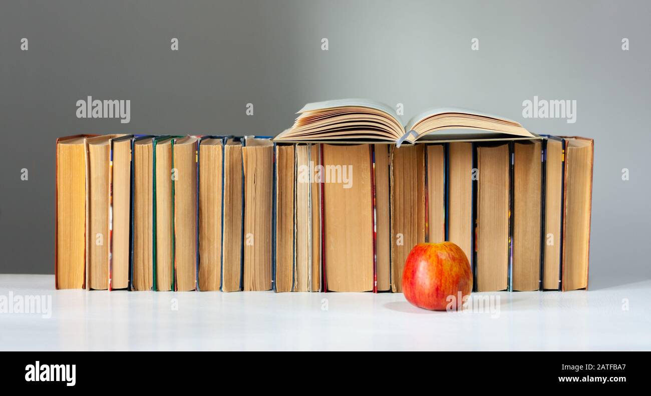 Open hardback book, diary, fanned pages on stack of books on white table with red apple. Books stacking. Back to school concept. Copy Space. Education Stock Photo