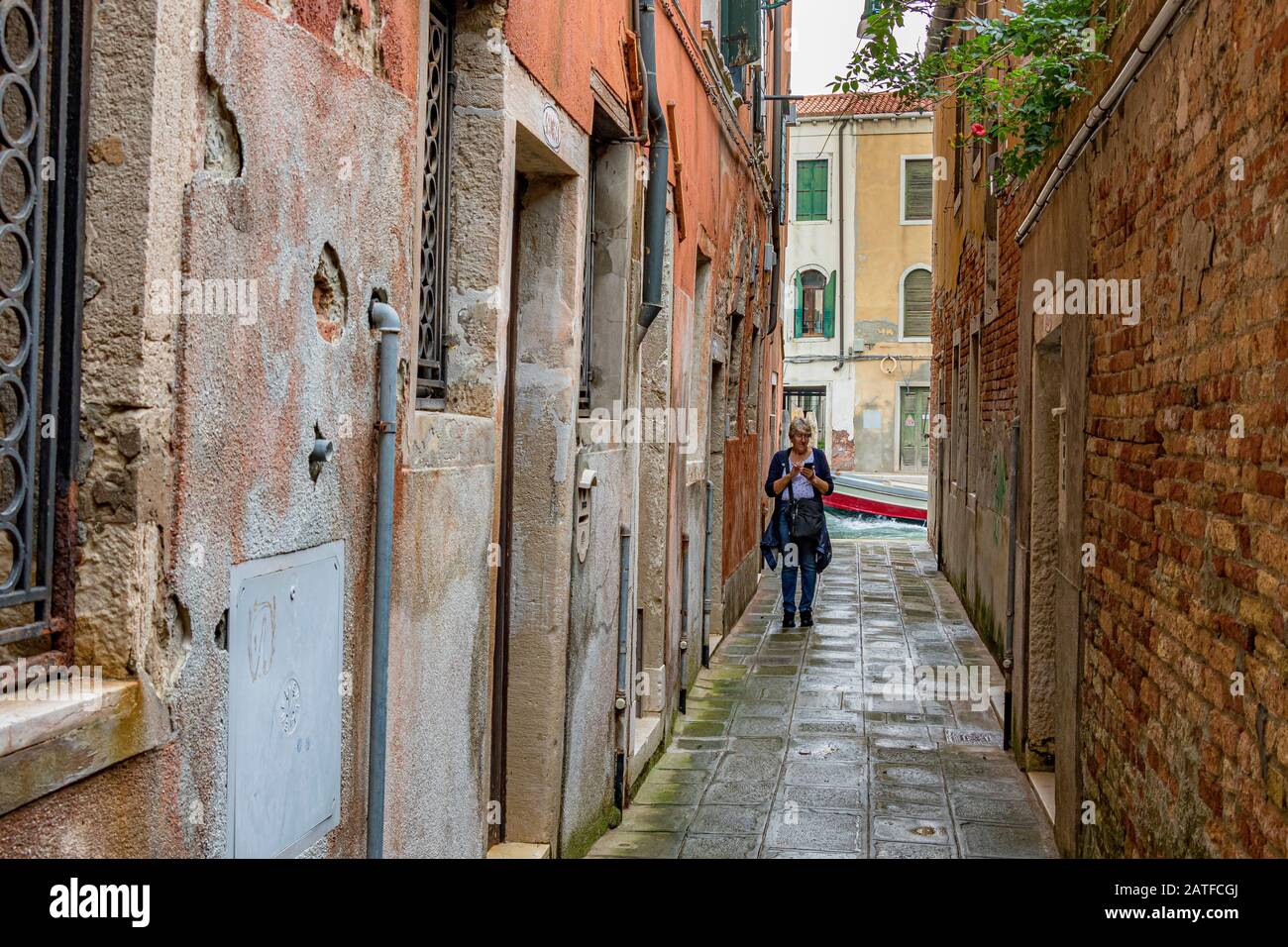 A woman walking down Calle dei Colori , a narrow alleyway which leads to a canal , in the Cannaregio district of Venice ,Italy Stock Photo