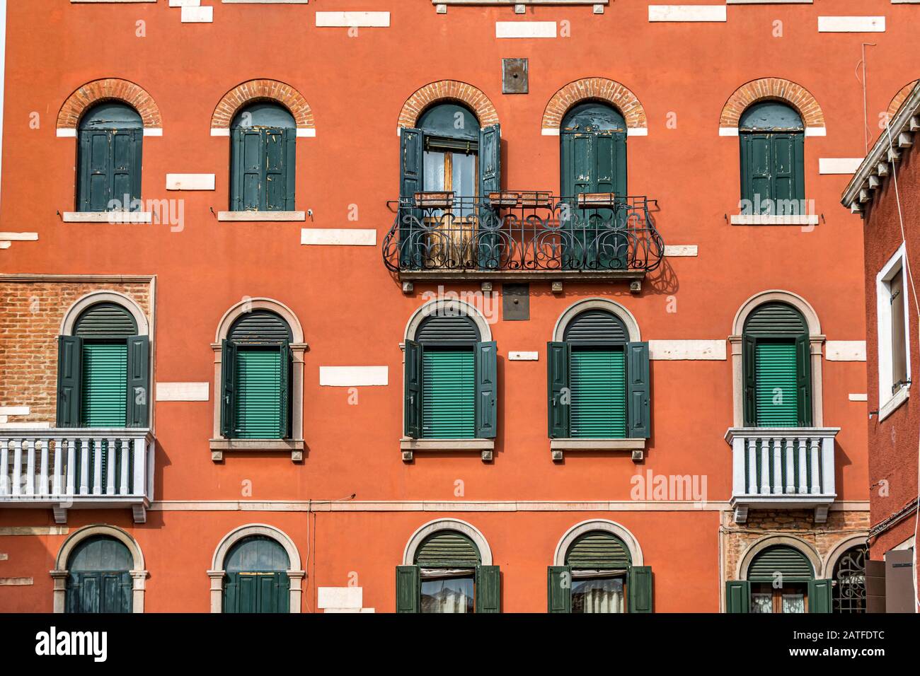 Close up of an orange coloured building with a wrought iron balcony and green shutters and windows with blinds in  C. Cappuccine Castello ,Venice Stock Photo