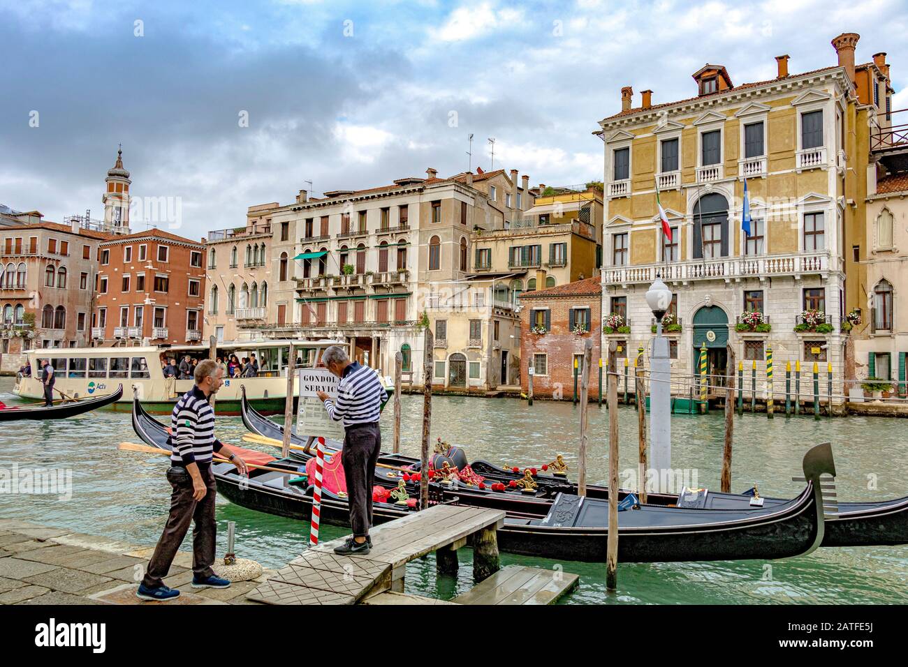 Two Gondoliers standing on a small jetty adjusting a sign along the Grand Canal in Venice ,Italy Stock Photo