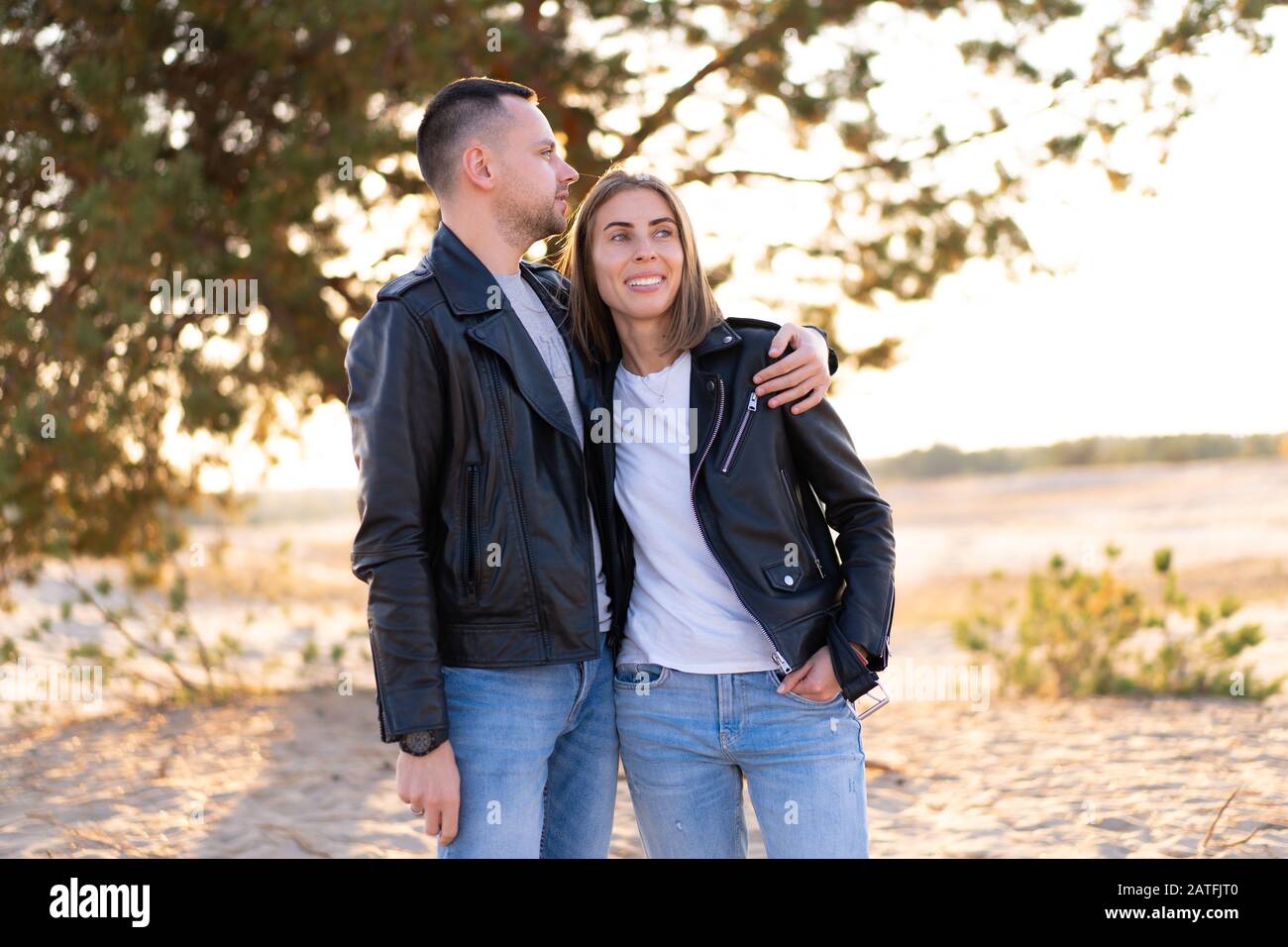 Happy and cute adorable adult couple leather jacket and jeans man with woman girlfriend walking, have fun play, laugh,smile and jump on sunset at dese Stock Photo