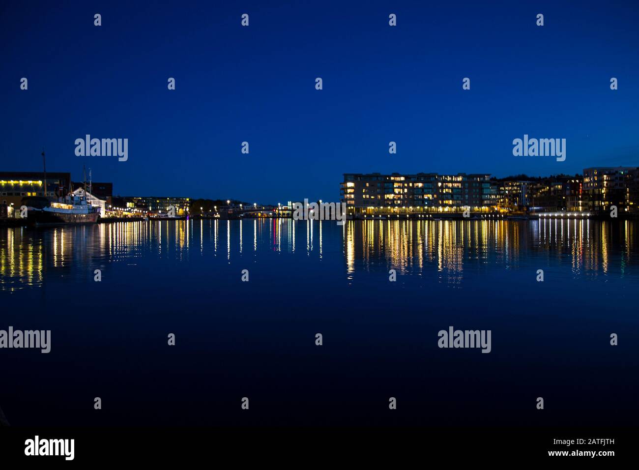 Night city lights reflecting on sea water, cityscape during the sunset. Stock Photo