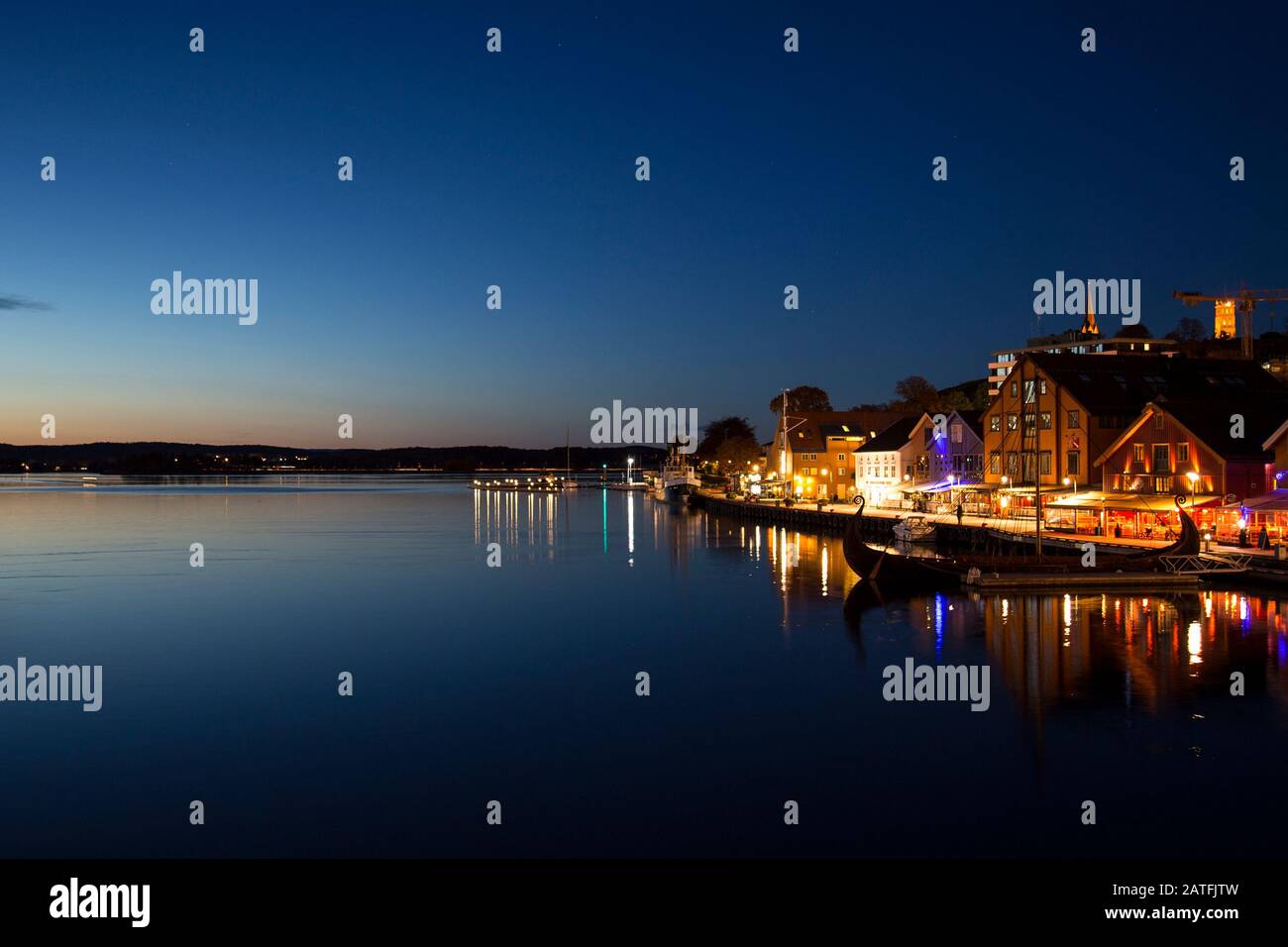 Amazing night shot of city harbour, port with viking ship with restaurants and bars. Sunset with blue sky and sea. Stock Photo