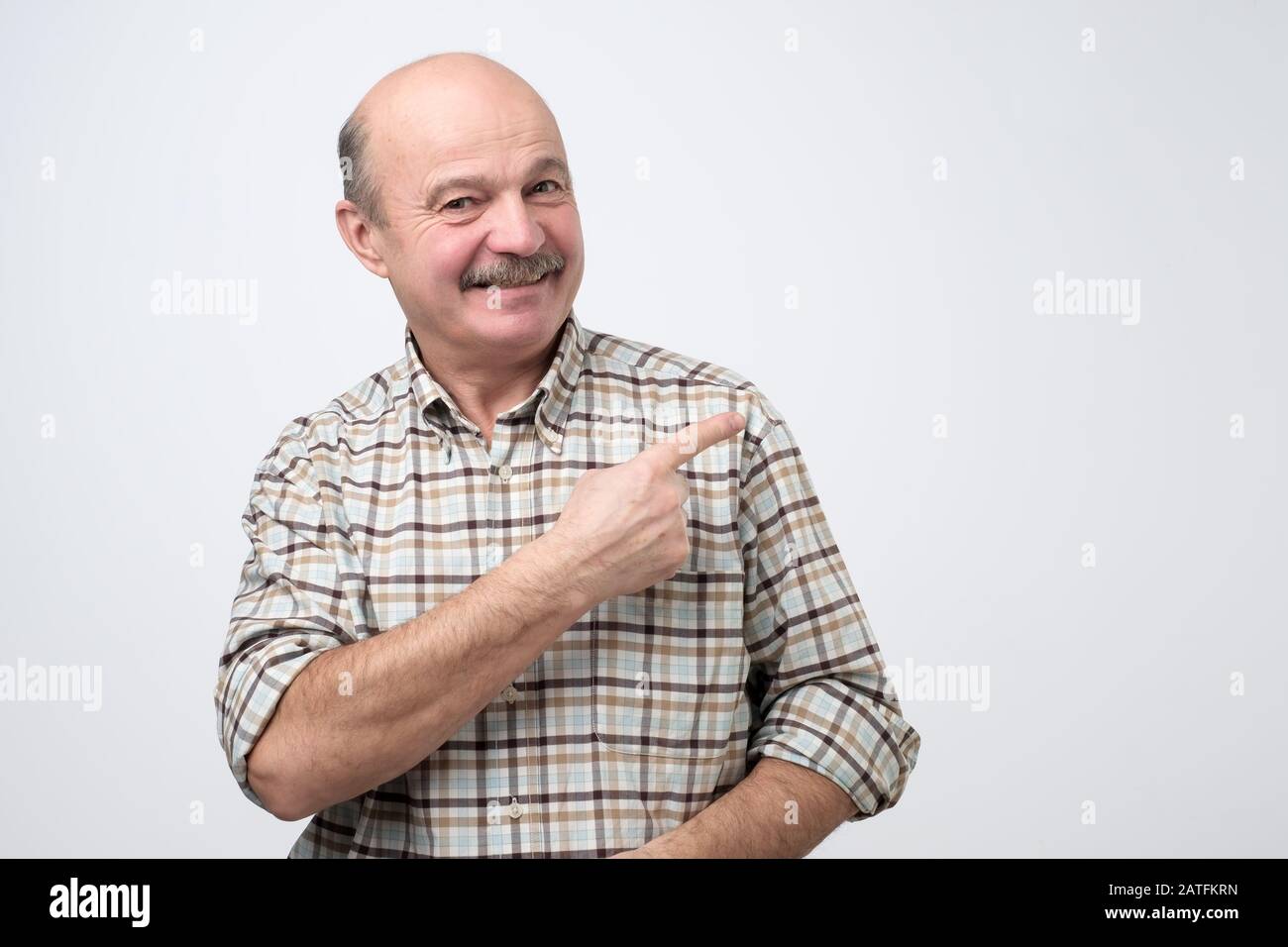 Confident senior man point away. Serious mature male gesturing with his finger aside. Studio shot Stock Photo