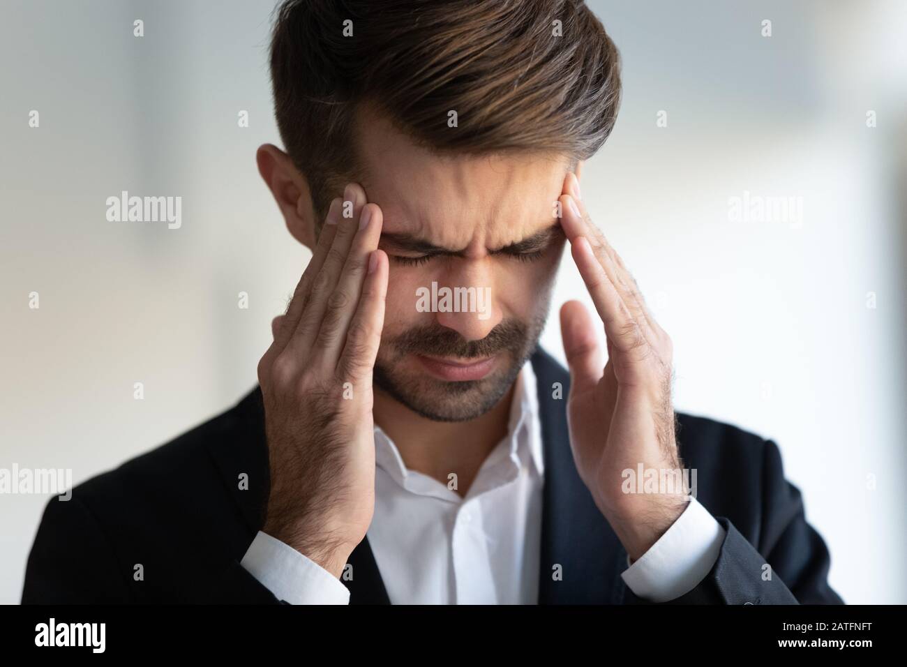 Businessman frown face closed eyes touches temples reduces migraine pain Stock Photo
