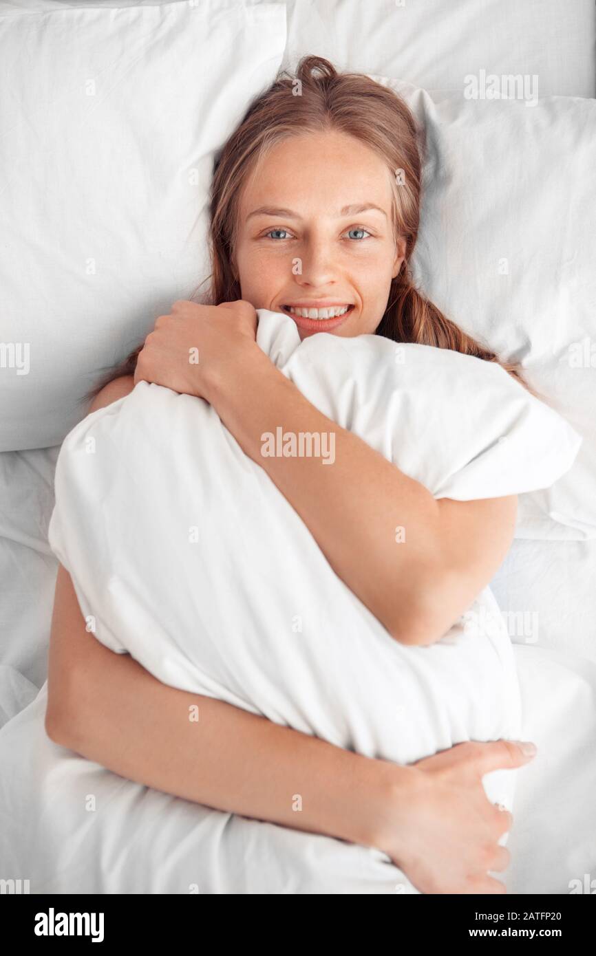 Morning at Home. Woman lying on bed hugging pillow smiling relaxed top