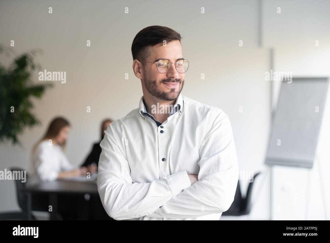 Smiling handsome businessman stands with arms crossed looking away ...
