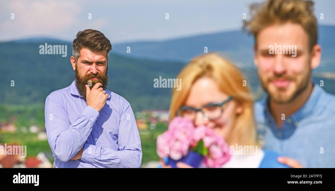 Lovers hugs outdoor flirt romance relations. Infidelity concept. Couple romantic date lovers bouquet flowers. Couple in love dating while jealous bearded man watching wife cheating him with lover. Stock Photo