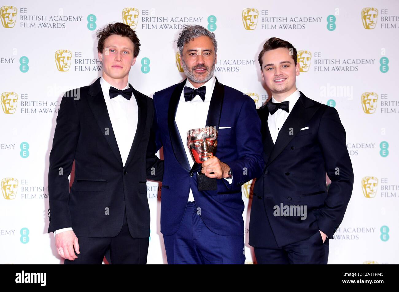 Charles Chapman and George MacKay pose for a phot with Taika Waititi after presenting him with the award for Best Adapted Screenplay in the press room at the 73rd British Academy Film Awards held at the Royal Albert Hall, London. Stock Photo