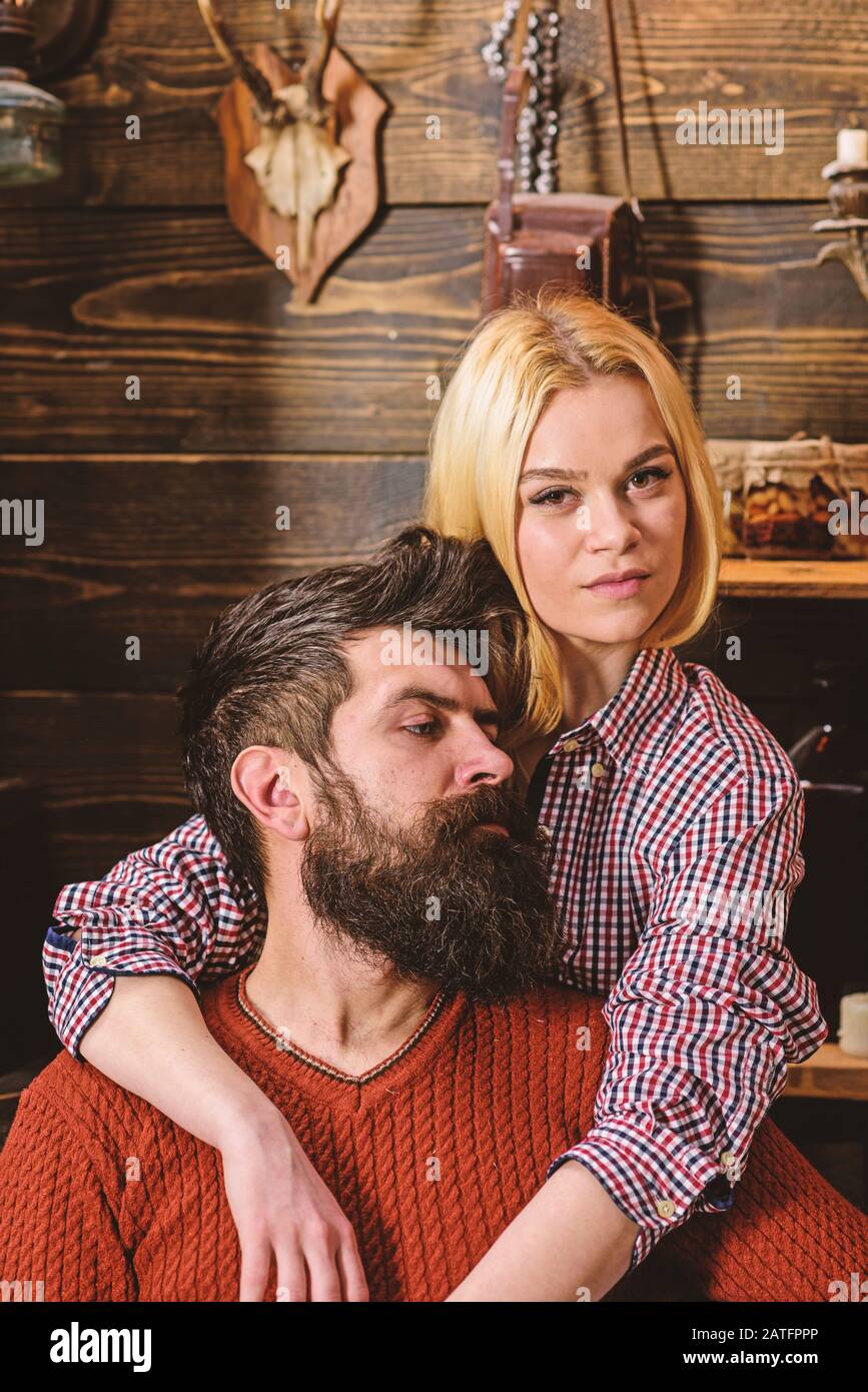 Couple in wooden vintage interior enjoy rest. Lady and man with beard on dreamy faces hugs. Couple in love spend romantic evening in warm atmosphere. Romantic evening concept. Stock Photo