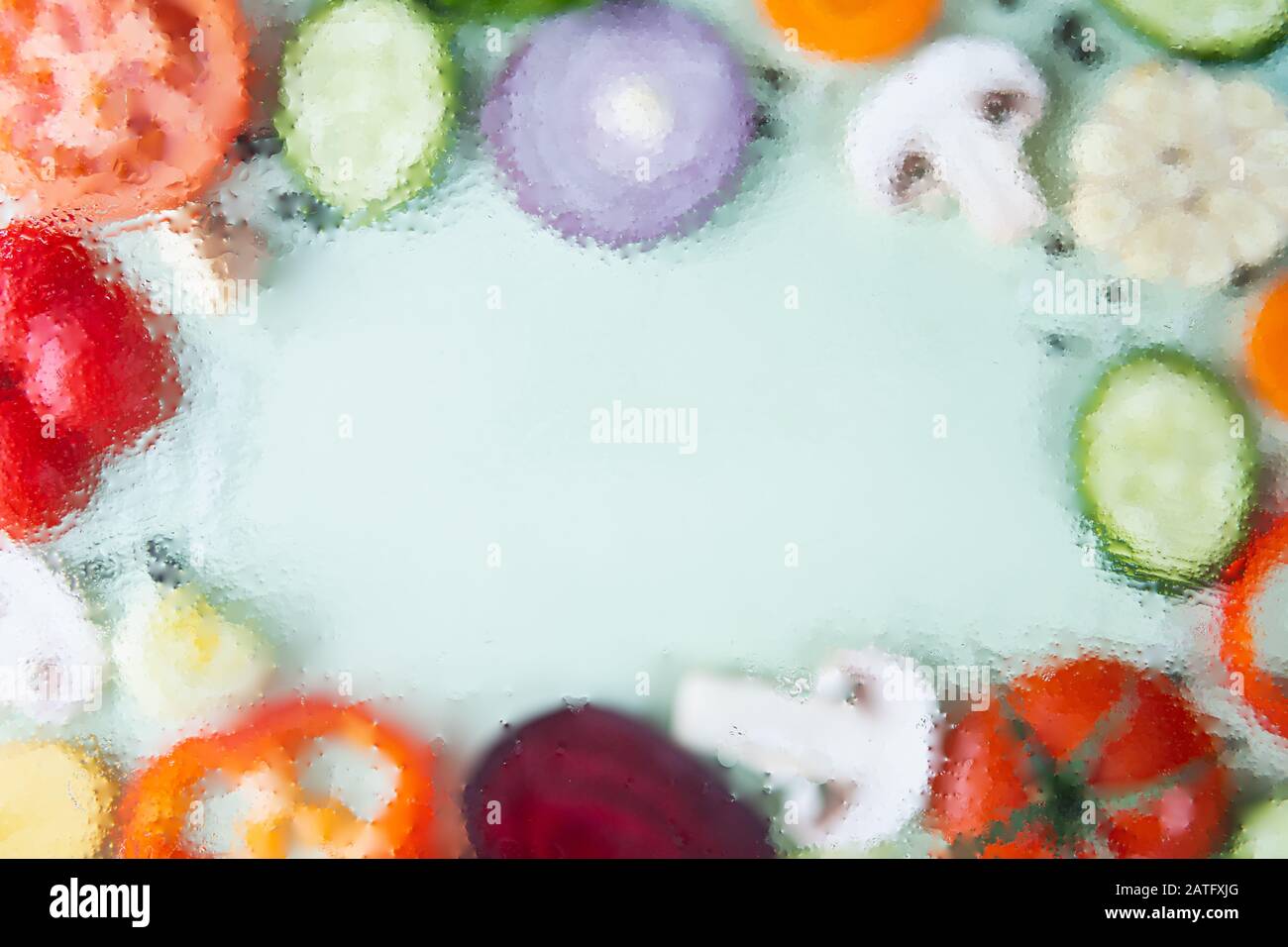 Assorted sliced vegetables on green background arranged in a frame with copy space in the middle. Out of focus image, water drops texture Stock Photo