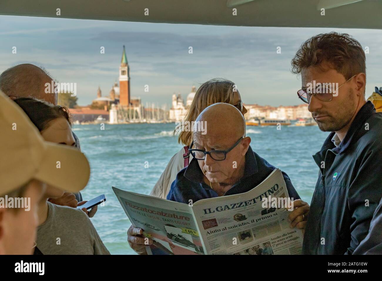 A man reading a newspaper standing next to other passengers on a Vaporetto or water bus service on The Venice Lagoon, on route to Venice ,Italy Stock Photo