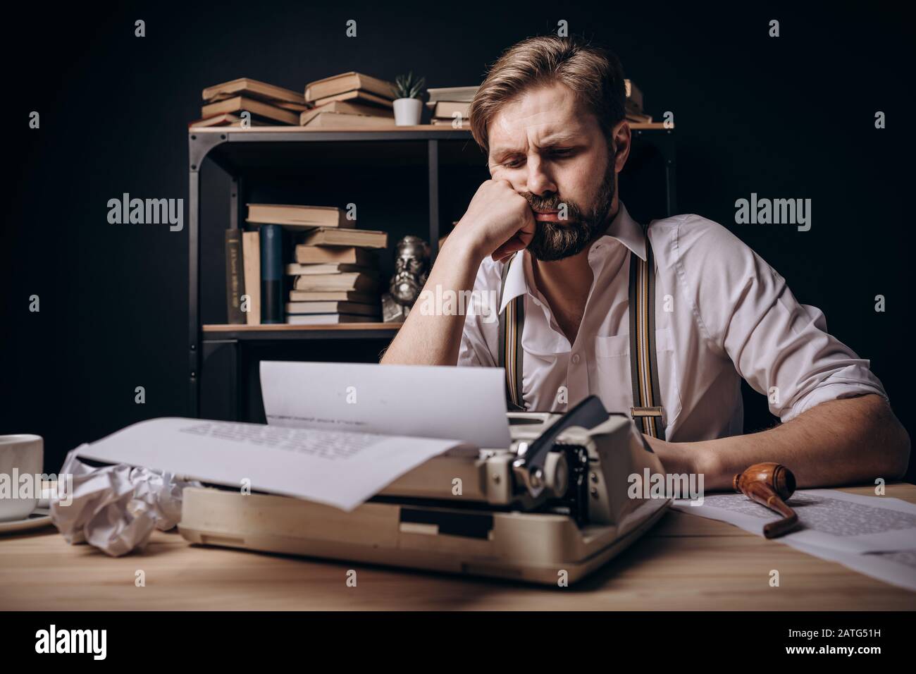 Thoughtful writer propping his chin up while sitting at his work desk Stock Photo