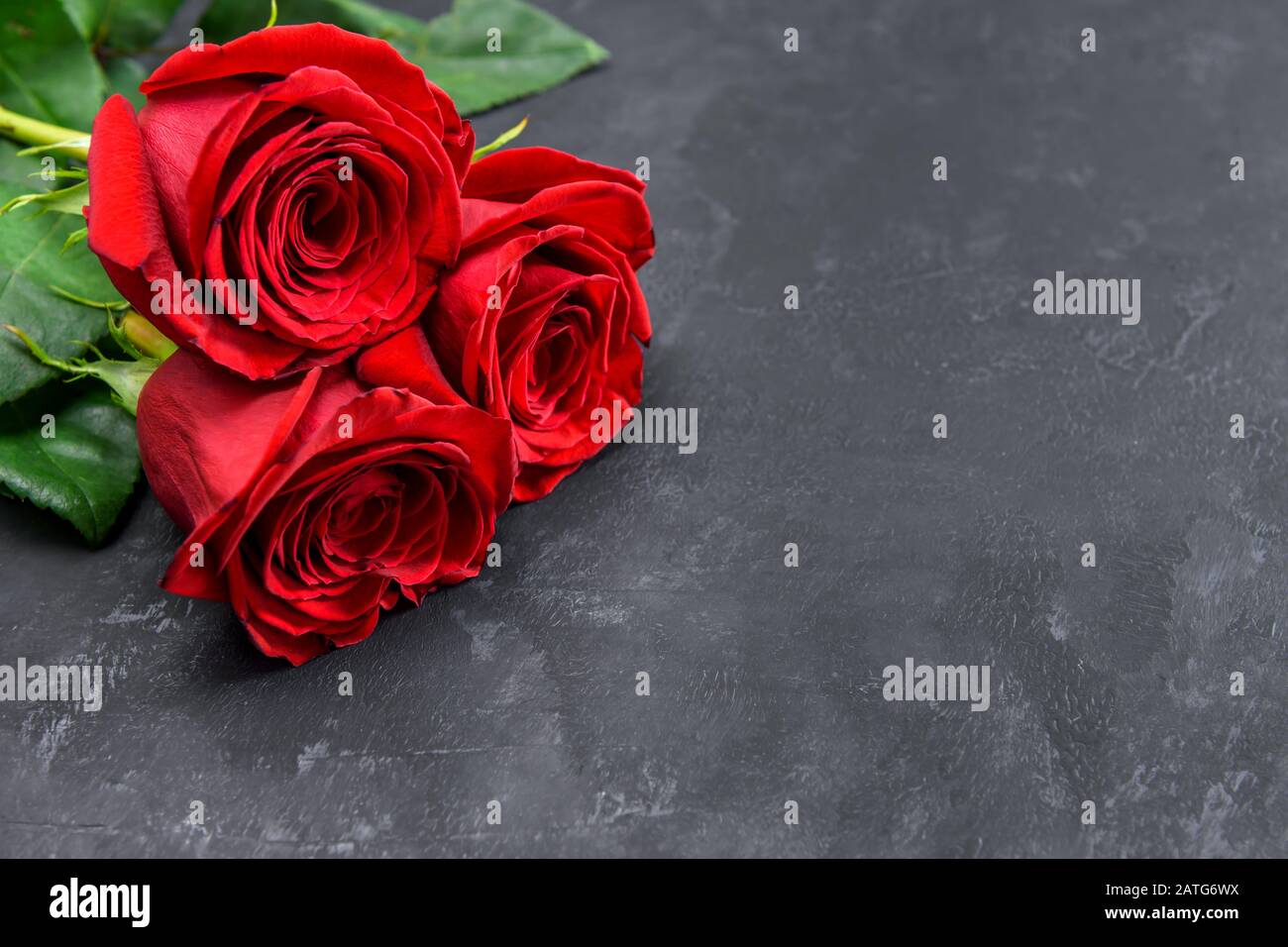 Three red roses on a dark table with copy space for text. Selective focus. Stock Photo