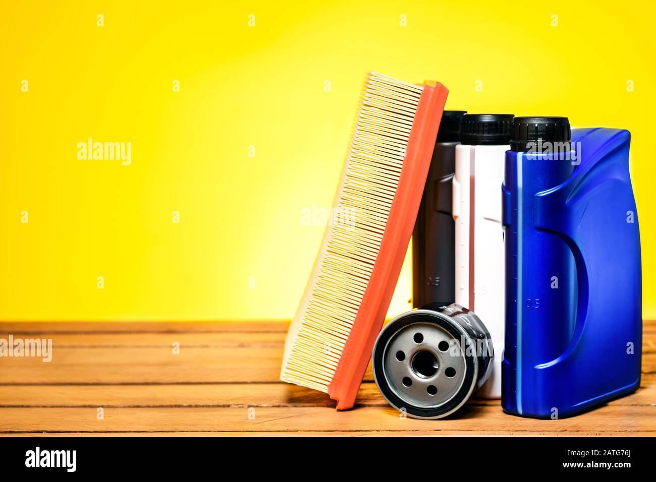 Spare parts for car service. Engine oil filter, air filter and three plastic oil and antifreeze cans on a wooden table in front of a yellow background Stock Photo