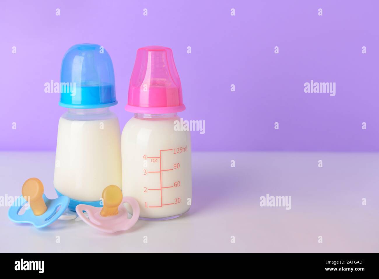 Bottles of milk for baby with pacifiers on color background Stock Photo