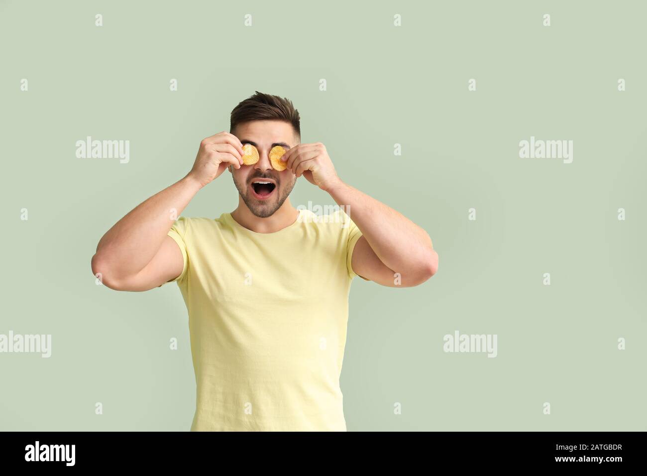 Funny young man with tasty potato chips on color background Stock Photo