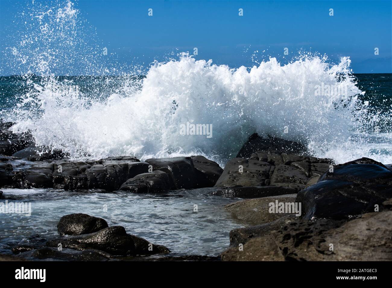 Waves crashing over the rocks creating a huge splash on a hot summers ...