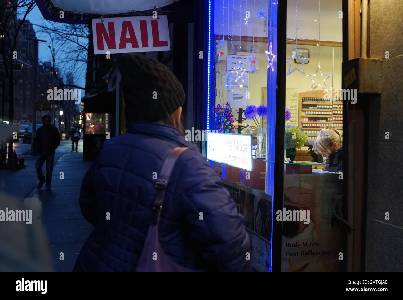 New York, NY / USA - December 29, 2019: Bundled woman prepares to treat herself and walk into a nail salon after work Stock Photo