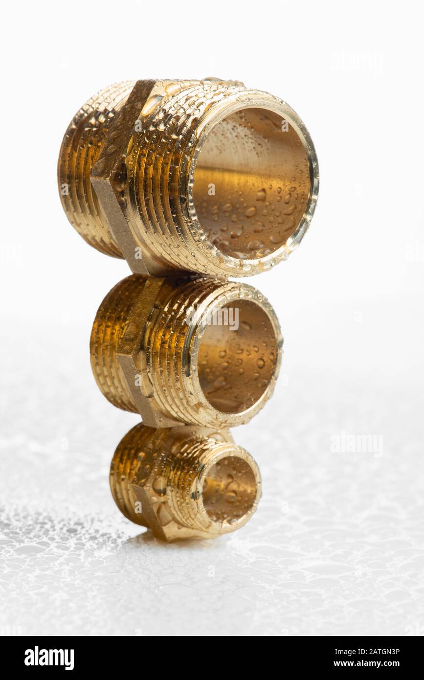 Closeup brass pipe fitting on white wet workshop table Stock Photo