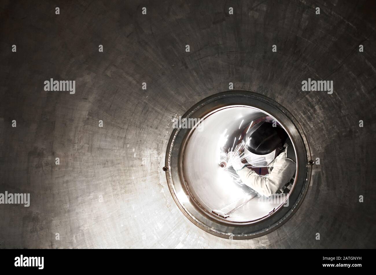 Welder or metal worker working inside a tunnel viewed down the length with receding perspective framing him as he works Stock Photo