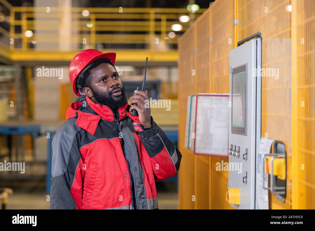 Serious bearded Black repairing engineer in hardhat using walkie-talkie while reporting on machine process Stock Photo