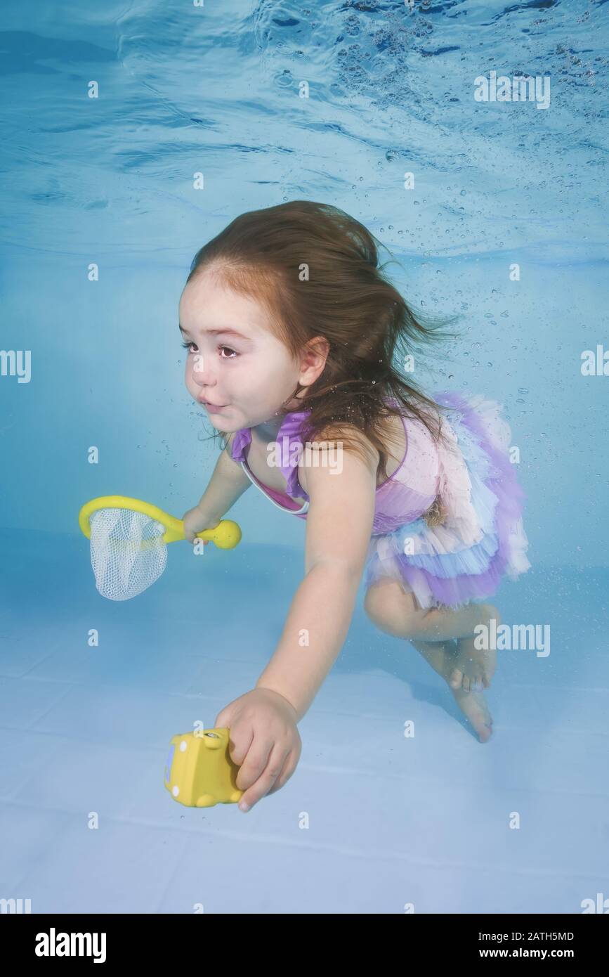 Girl plays with toys underwater in a swimming pool Stock Photo