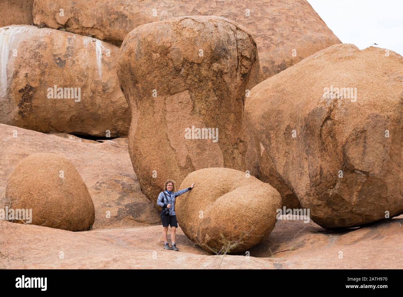 Young woman standing next to bizarre boulders and rock formations in the nature reserve of Spitzkoppe, Erongo, Namibia, Africa Stock Photo
