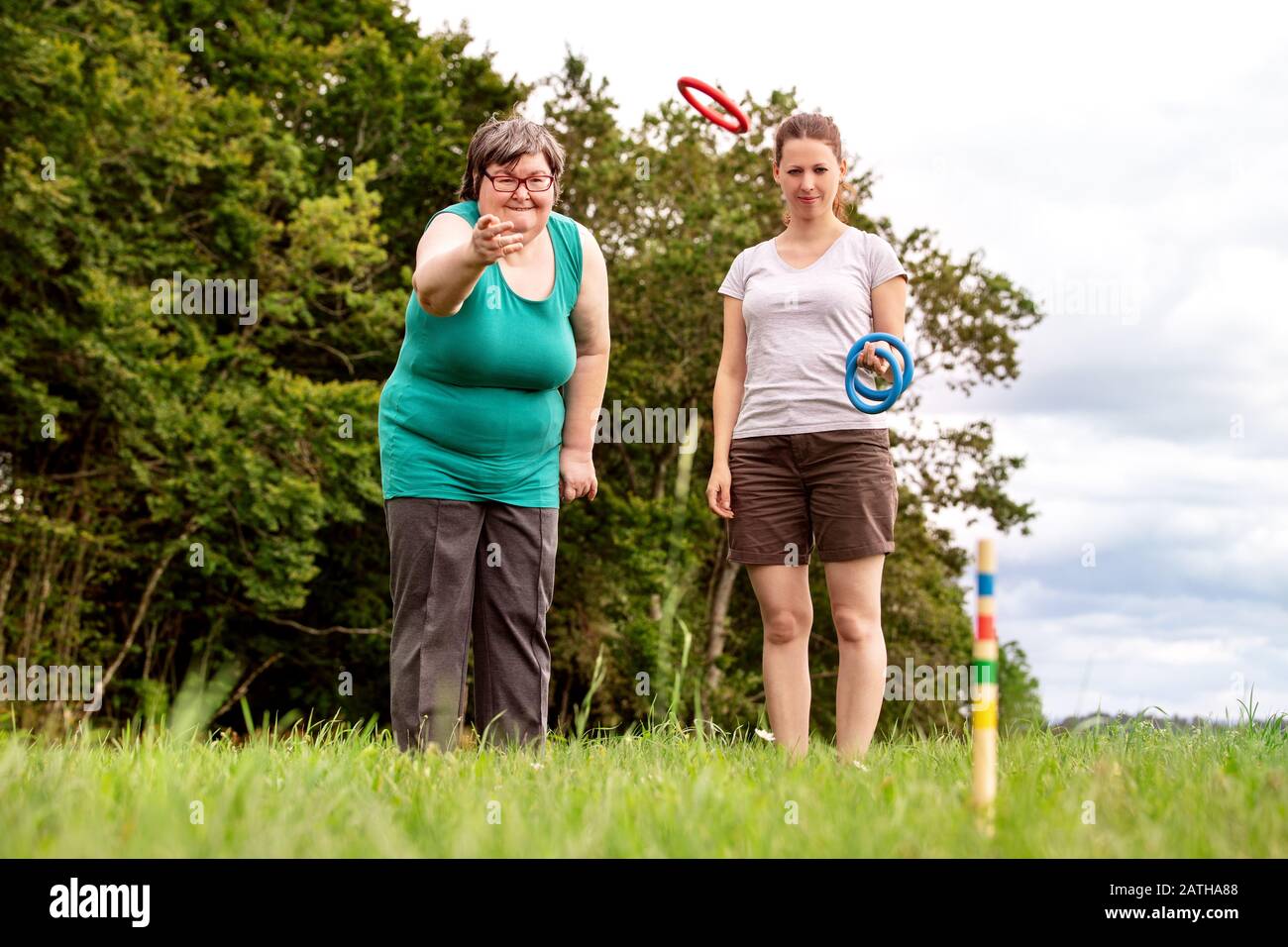 mental disabled woman is playing a game to train her motor abilities, exercises with a friend or therapist outdoors on a meadow Stock Photo