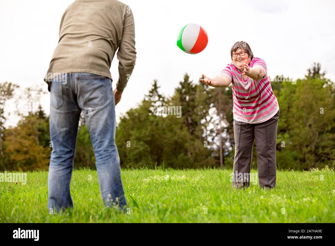 mental disabled woman is throwing a ball to a man to train her motor function, exercises with a friend or therapist outdoors on a meadow Stock Photo