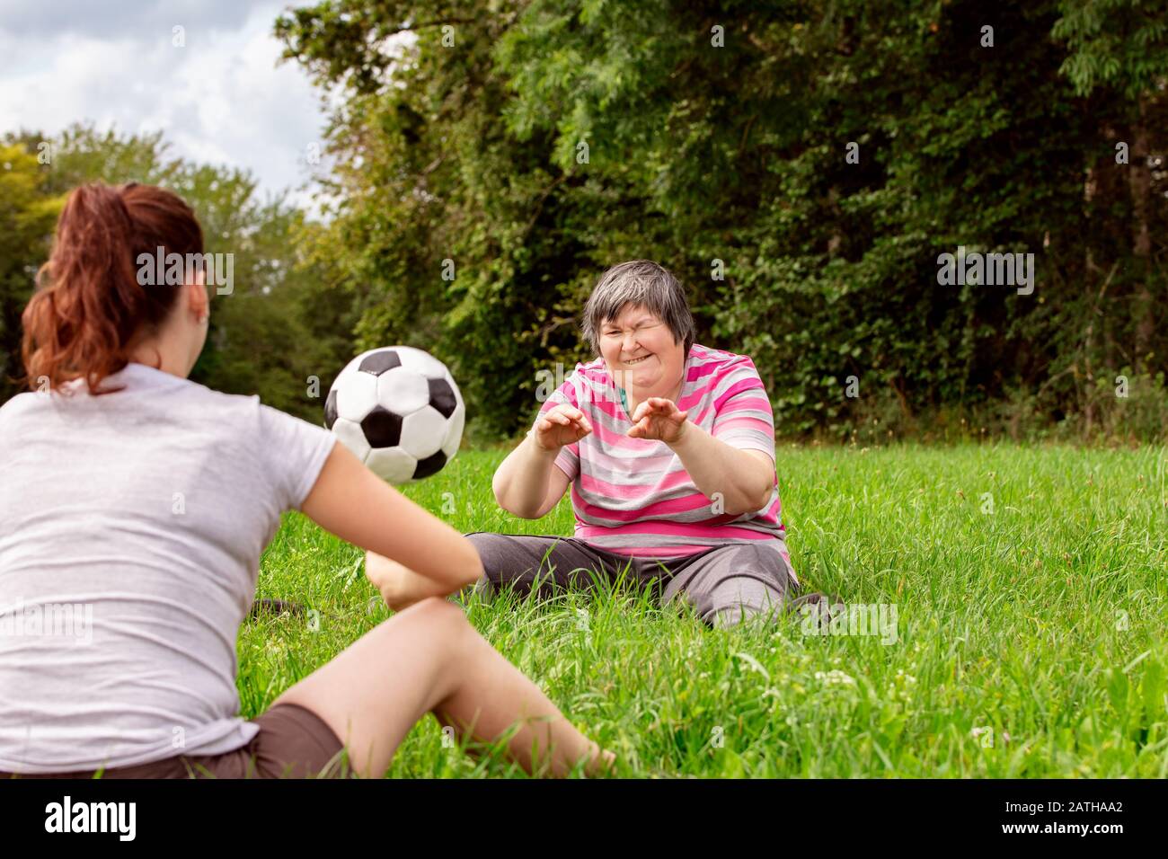 mental disabled woman is throwing a ball to a woman to train her motor function, exercises with a friend or therapist outdoors on a meadow Stock Photo
