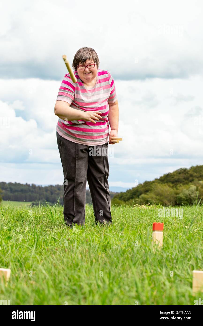 mental disabled woman is playing kubb to train her motor abilities, funny exercises outdoors on a meadow Stock Photo