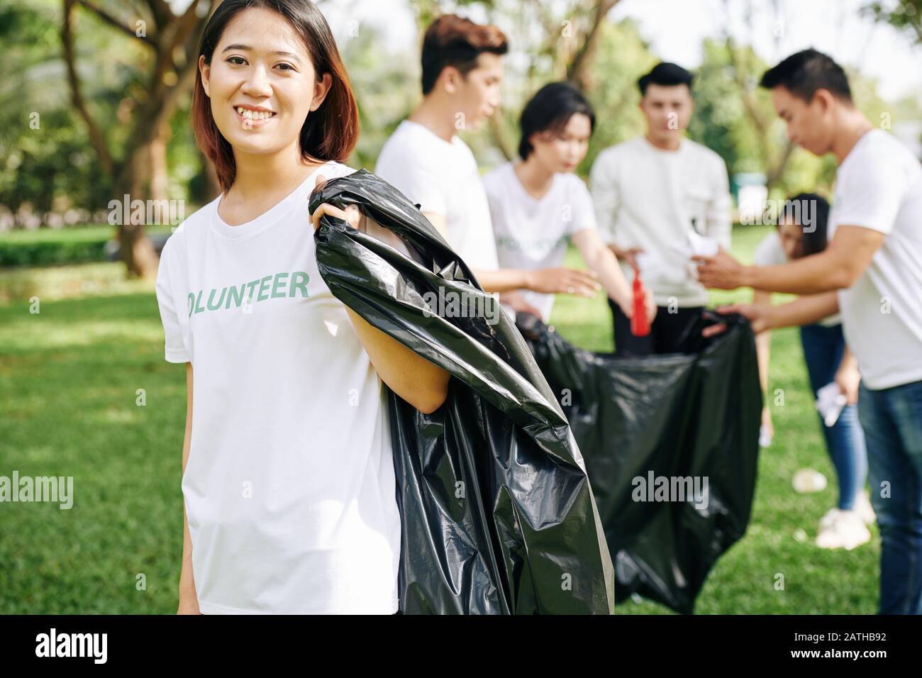 Portrait of young happy volunteer with big plastic trash bag for collecting garbage in park Stock Photo