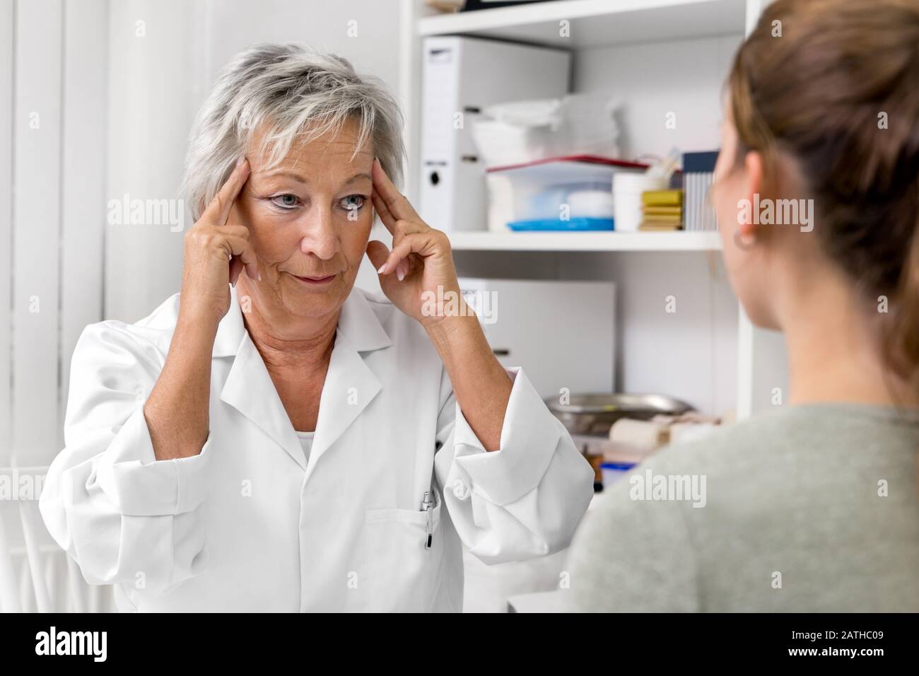 Female doctor holding her temporal, demonstration of headache or neuralgia pain, medical office Stock Photo