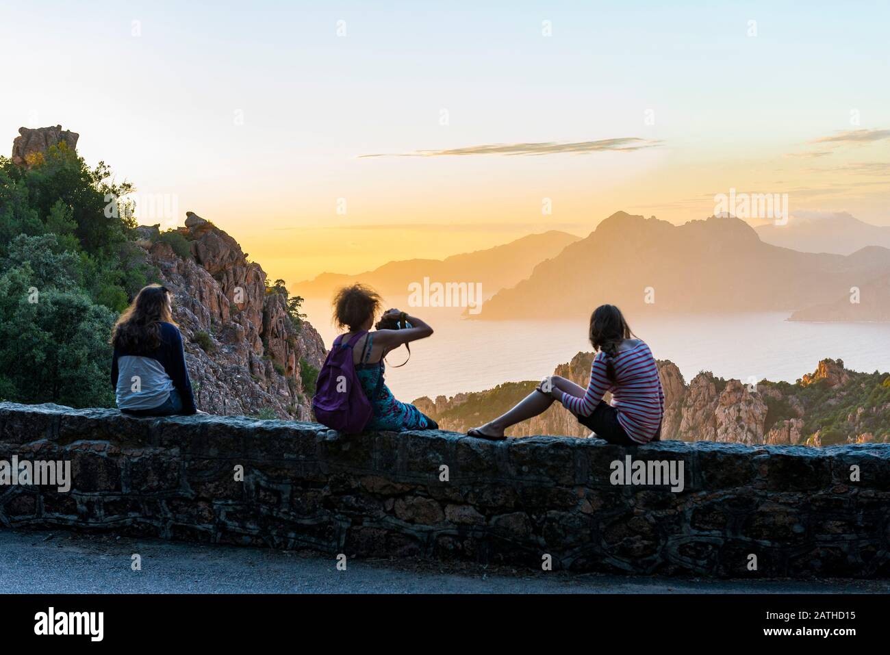 France. Corse. Corsica. Calanques de Piana. Au coucher de soleil, trois touristes admirent le panorama devant elles. : la mer Méditerranée et les roch Stock Photo