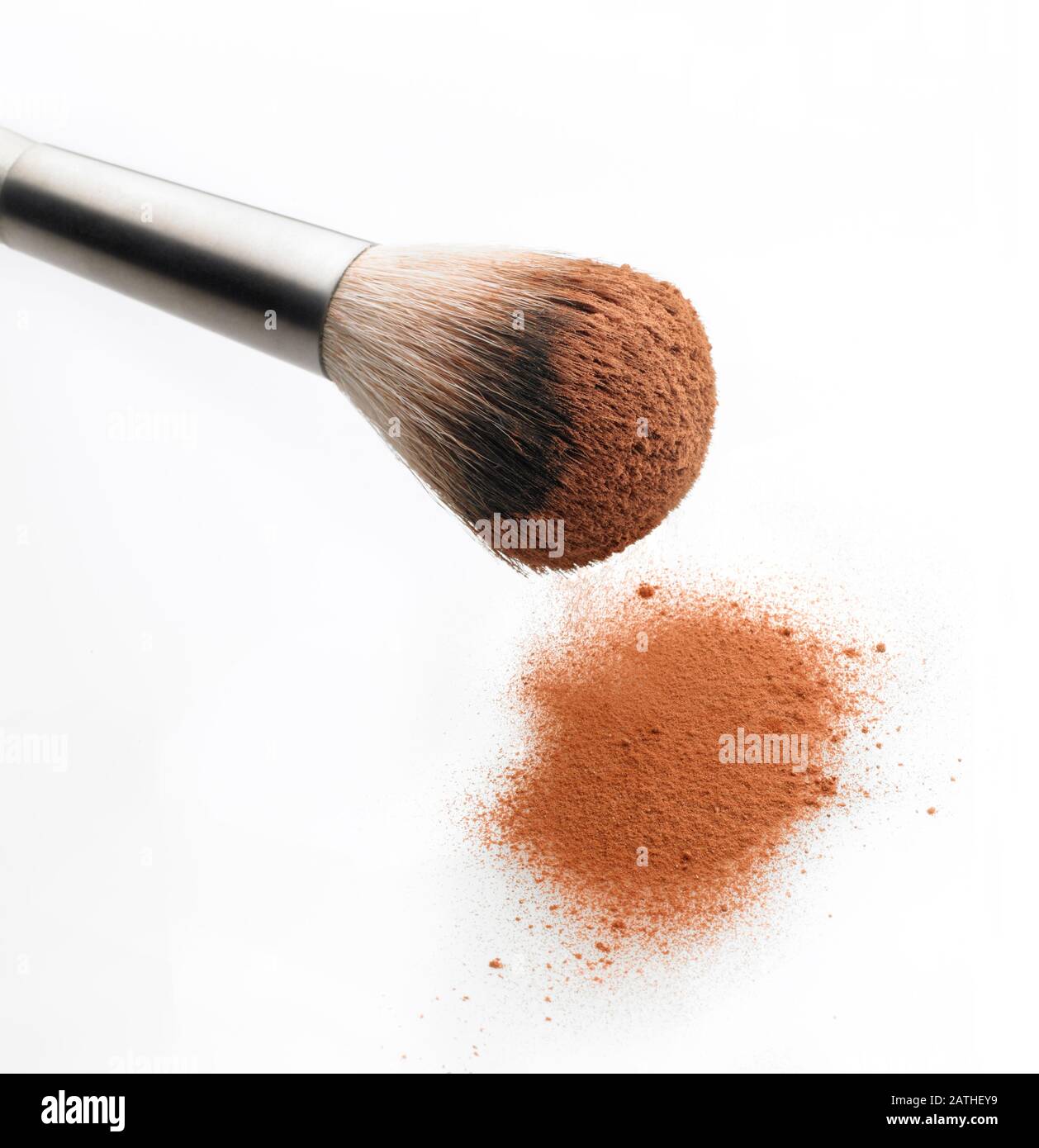 Close Up view of brush removing makeup powder from a pile. White background. Stock Photo
