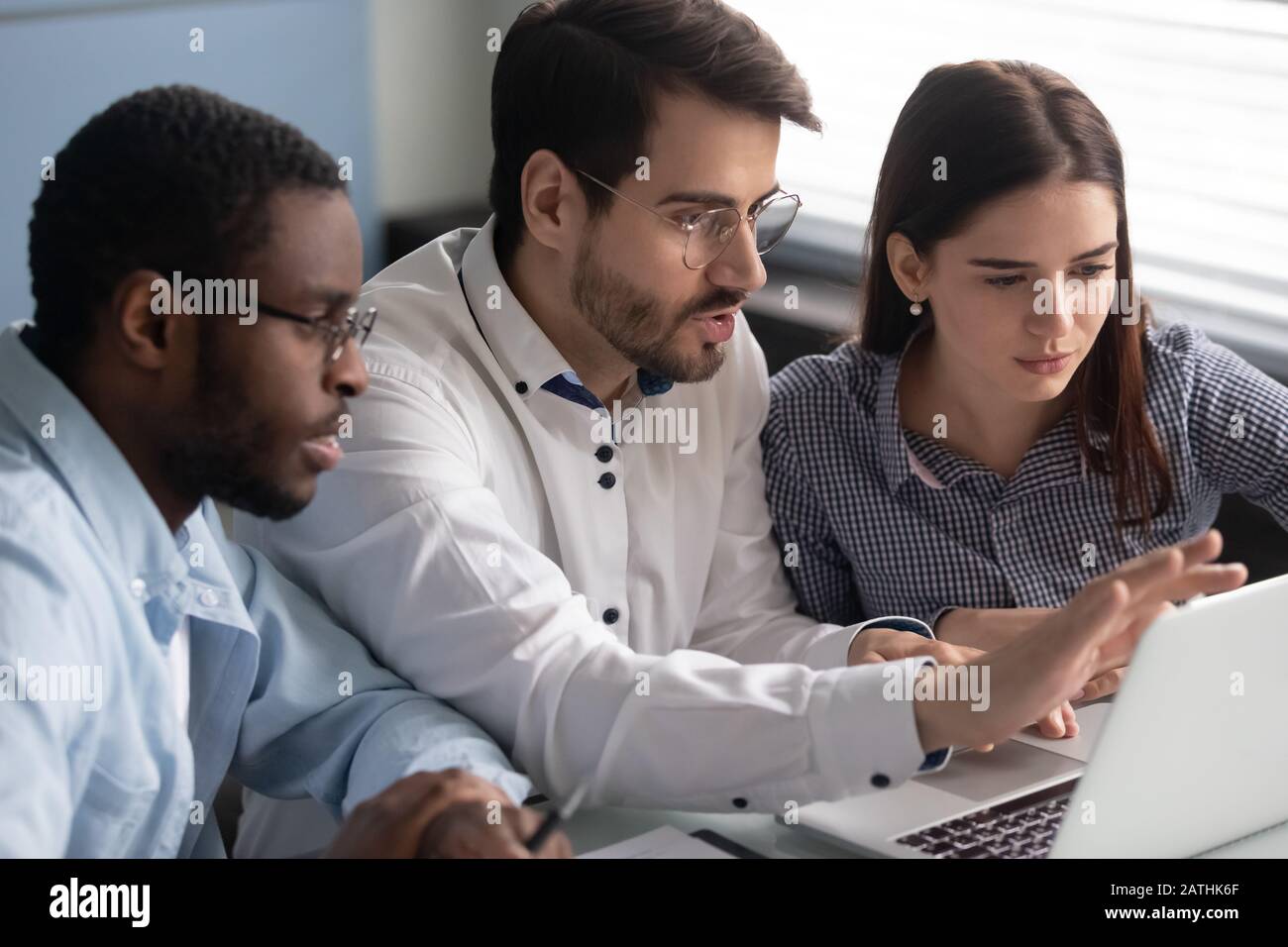 Three diverse colleagues looking at laptop screen working together indoors Stock Photo