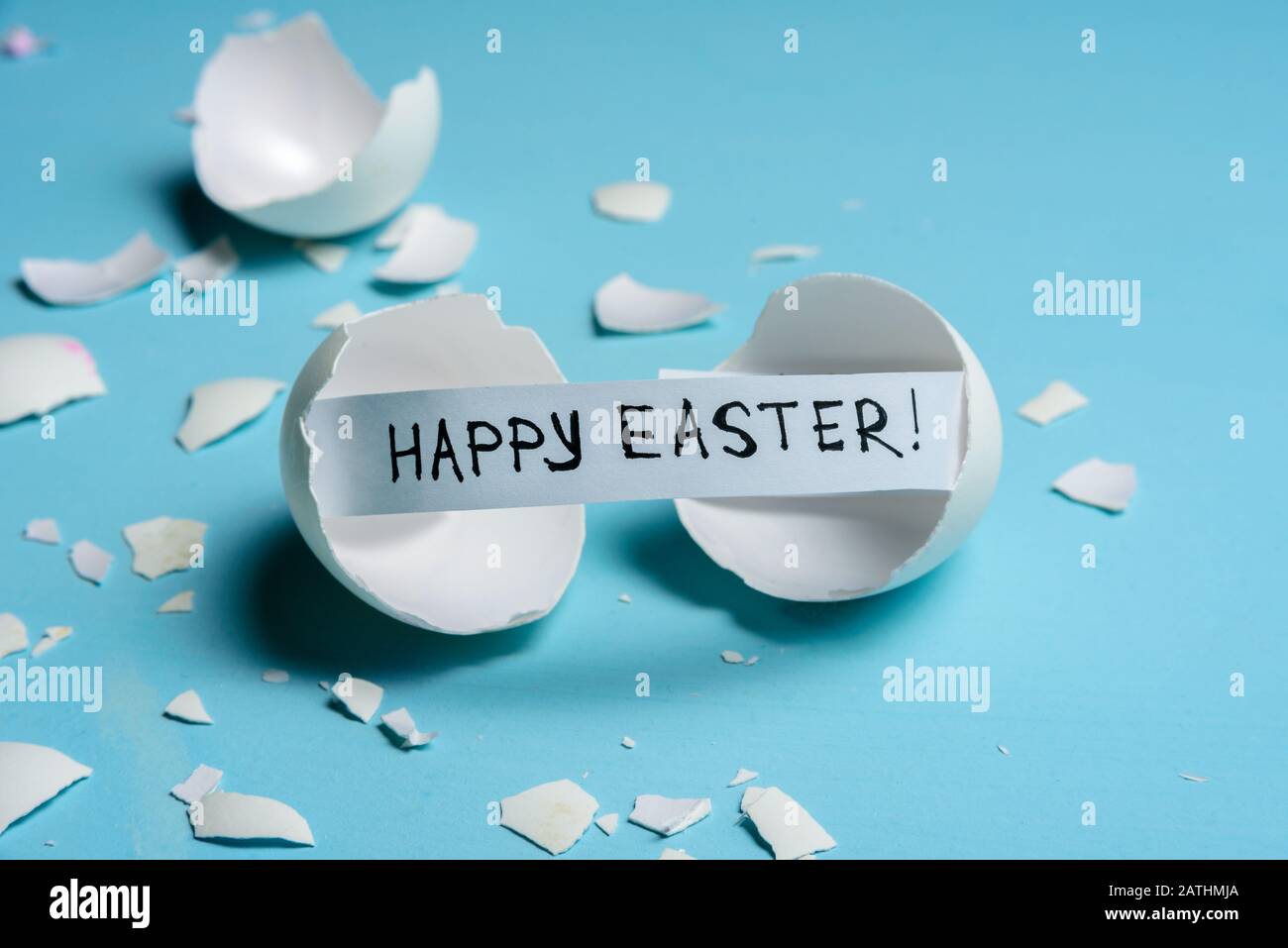 Cracked egg with text HAPPY EASTER on light blue background. Copy space Stock Photo