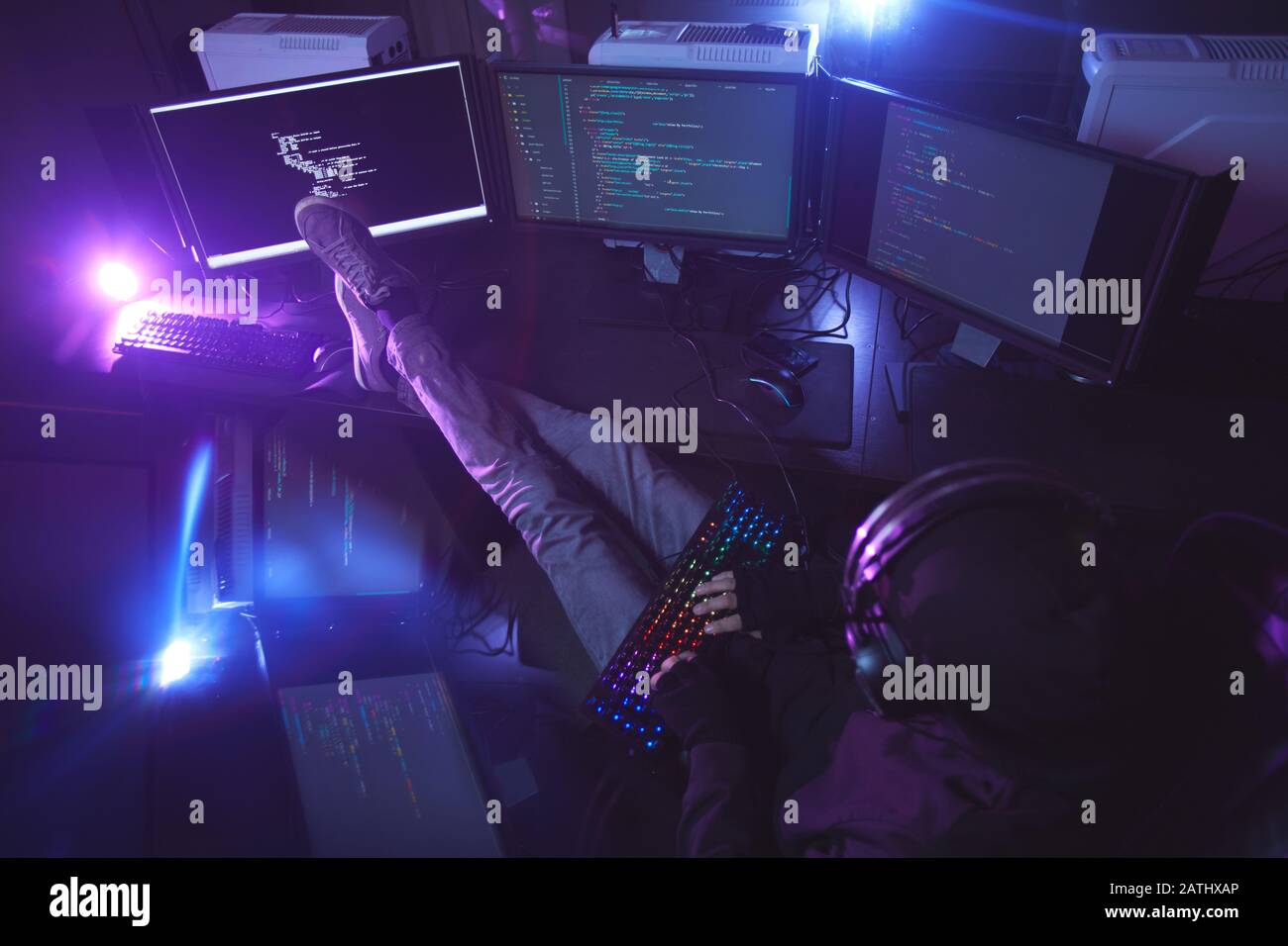 Top view at young man surrounded by multiple screens programming or hacking security in dark room, copy space Stock Photo