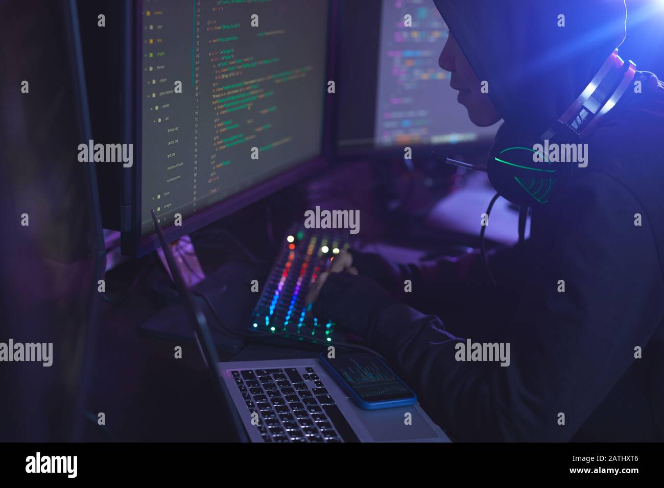 Side view at unrecognizable cyber security hacker wearing hood while working on programming in dark room, copy space Stock Photo