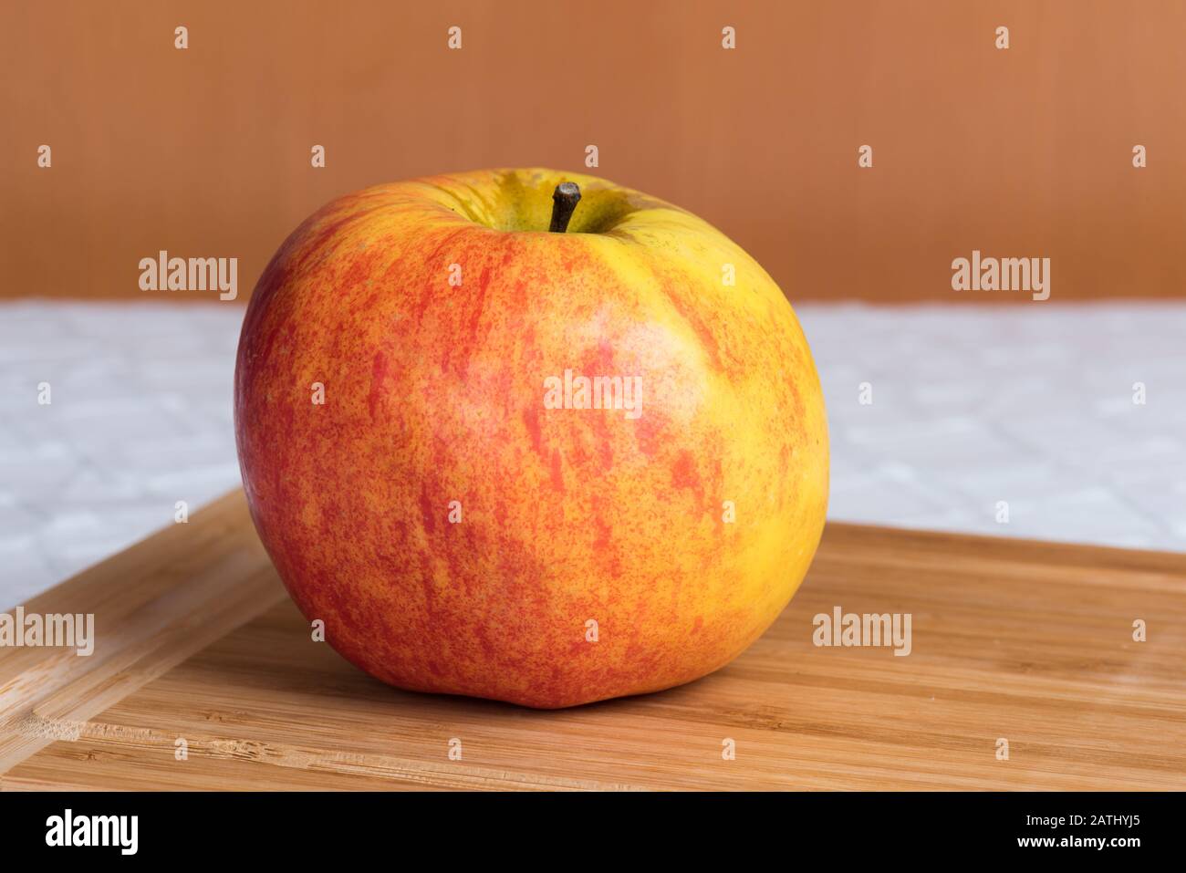 A ripe apple (malus domestica) is lying on a wooden board on a kitchen table. Stock Photo