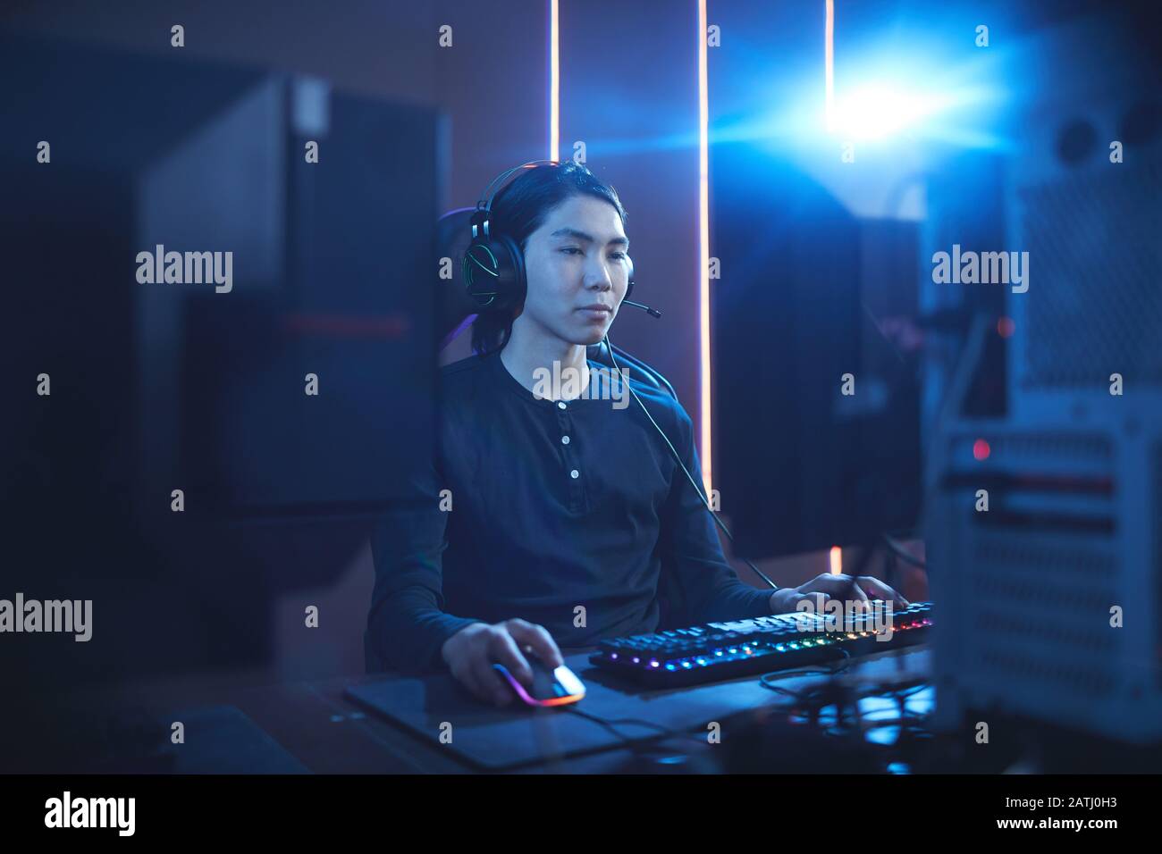 Portrait of young Asian man using computer in dark cyber interior with ...