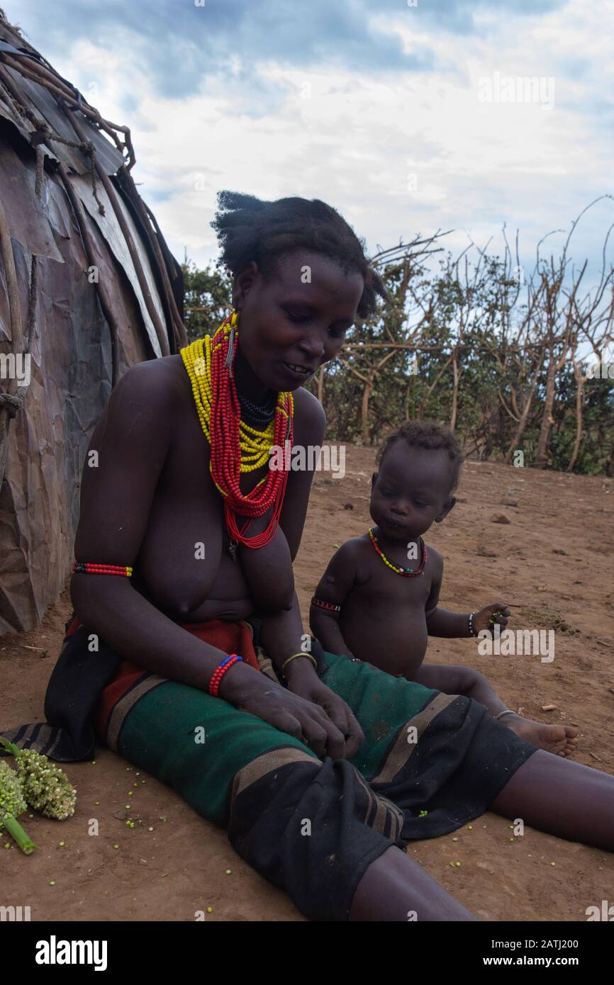 Omorate, Ethiopia - Nov 2018: Woman of Dassanech tribe with kid in front of the tribal house. Omo valley Stock Photo
