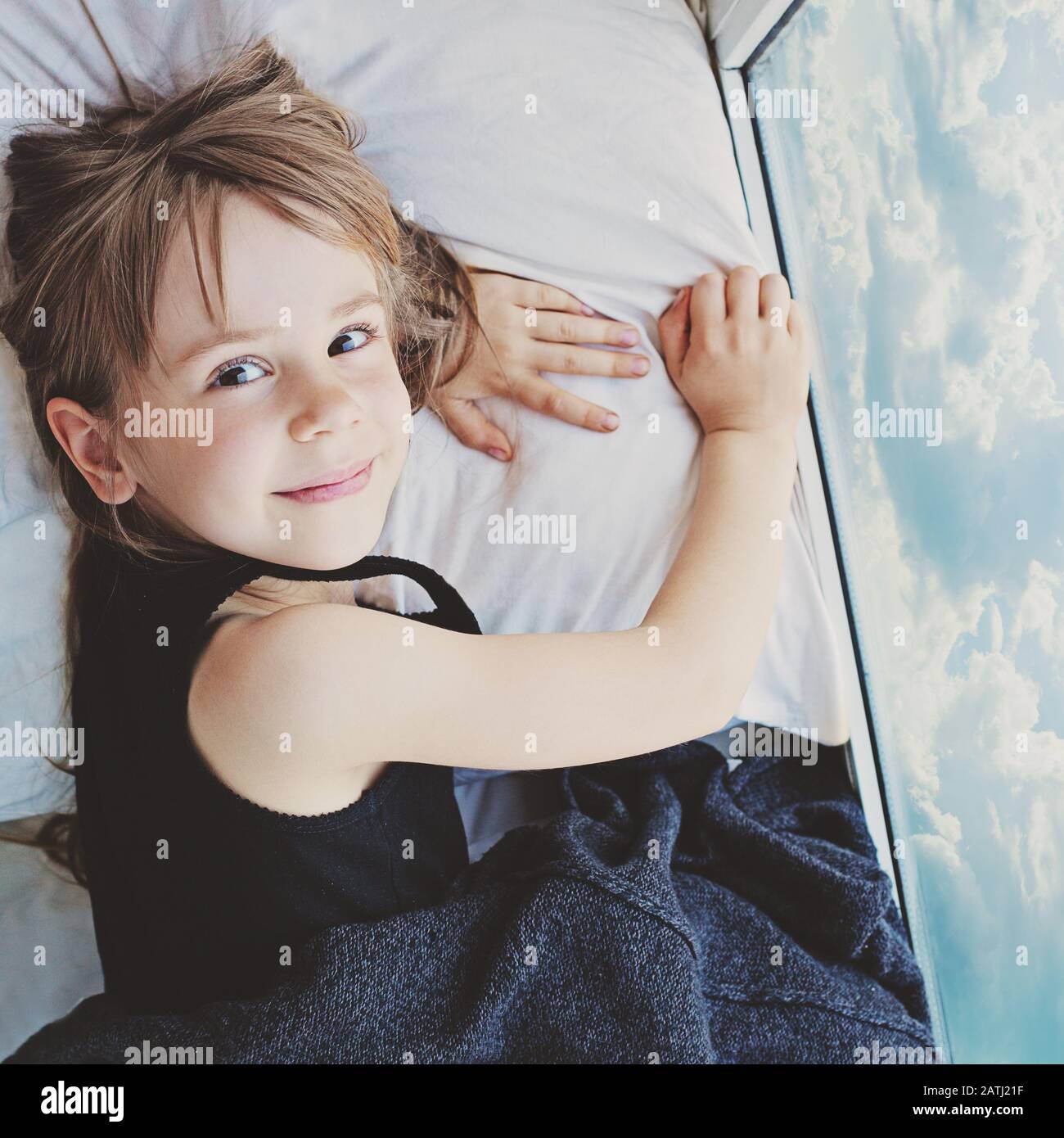 Carefree child girl dreaming near window with sky clouds Stock Photo ...