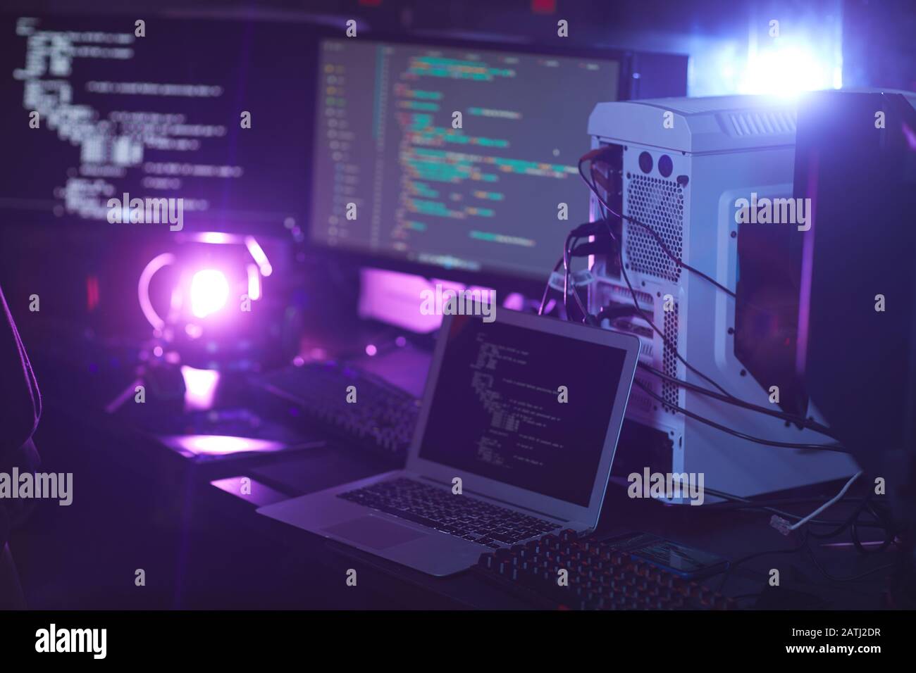 Background image of various computer equipment with programming code on screens in dark room, cyber security concept, copy space Stock Photo